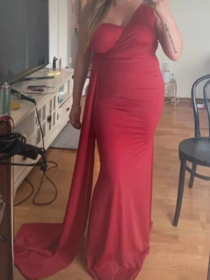 Röd oneshoulder långklänning - Snygg röd långklänning med oneshoulder-design. Klänningen har en elegant släp och figurnära passform. Stretch material