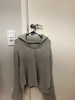 Grå ribbstickad tröja med dragkedja - Mysig grå stickad tröja med halv dragkedja framtill och bred krage. Tröjan har långa ärmar och är ribbstickad för extra struktur. Materialet känns mjukt och följsamt. Köpt på VEROMODA. Mycket bra skick!