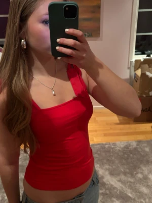 Röd linnetopp med rosettband - Snygg röd linnetopp med smickrande passform och breda axelband som knyts i rosetter på axlarna. 