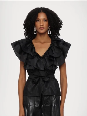 Svart volangblus med knytband - Supersnygg svart blus med stora volanger längs axlar och bröst, samt knytband i midjan. Djup v-ringning och korta ärmar ger en trendig look. Perfekt för dig som vill sticka ut med en statement-topp. Köpt på Åhléns för 2700kr🤎🤎