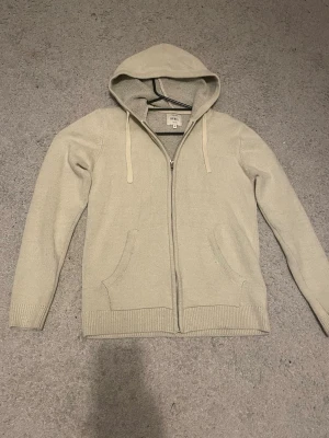 Beige hoodie med dragkedja från Rebel - Säljer en beige hoodie från Rebel med dragkedja framtill och två fickor. Hoodien är stickad i ett otroligt skönt och mjukt material. Perfekt för chill dagar och enkel att matcha med ett par jeans! Pris ej hugget i sten. Skriv om ni har frågor!