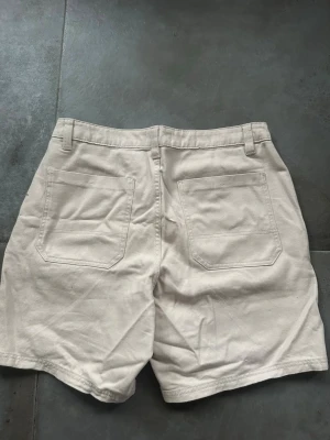 Beiga högmidjade bomullsshorts nya  - Snygga beiga shorts i bomull med hög midja och raka ben. Shortsen har två stora bakfickor och hällor för bälte. Perfekta för varma dagar och enkel att matcha med olika stilar.