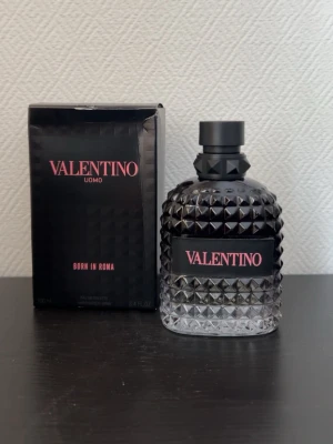 Valentino Uomo Born In Roma EdT - Valentino Uomo Born In Roma är en parfym med en lyxig, svart och transparent glasflaska med nitar och svart kork. Märket och doftnamnet syns i rosa text på både flaskan och kartongen. Flaskan har en modern, edgy design som sticker ut.