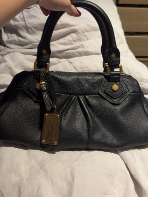 Svart Marc Jacobs handväska  - Säljer min sjukt snygga Marc Jacobs väska. Den är inprincip helt oanvänd och köpt av mig inne på deras butik. Kvitto och dustbag medkommer. 
