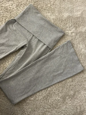 Grå leggings från Stradivarius - Säljer ett par ljusgrå leggings från Stradivarius med bred midjeresår och bootcut. Tillverkade i mjukt och stretchigt material som sitter skönt på kroppen. Perfekta för en avslappnad och trendig look.
