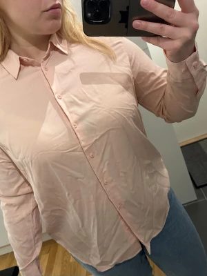 Ljusrosa skjorta ny - Klassisk ljusrosa/peach skjorta med lång ärm och  i ett tunt, mjukt material som känns skönt mot huden. Säljer pga den färgnyansen passar inte mig. Helt ny, oanvänd. Nypris 449kr (rayon blouse) 