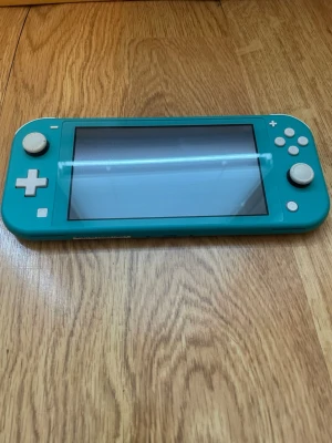 Turkos Nintendo Switch Lite konsol - Säljer en turkos Nintendo Switch Lite, en smidig och portabel spelkonsol med inbyggda kontroller och stor skärm. Konsolen är tillverkad i plast och har vita knappar och styrspakar. Perfekt för gaming på språng och enkel att ta med överallt. Säljes med zelda spel och laddkabel.