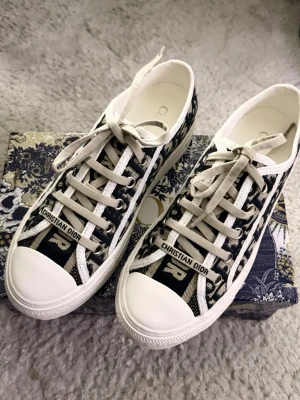 Christian Dior Oblique sneakers - Snygga låga sneakers från Christian Dior med klassiskt blått och vitt oblique-mönster. Skorna har vita gummisulor, beige snörning och tydlig logga på sidan och tungan. Tillverkade i canvas med detaljer i gummi. Perfekta för dig som vill ha en lyxig och trendig look. Helt nya skor perfekt skick!