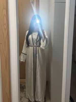 Vit abaya  - Vit abaya storlek 56 kan sägas passar för XS-S. Underklänning sedan koftan och en bälte plus vit slöja kommer med även. Perfekt för nikkah och andra tillfällen. Använd endast en gång. Ser skrynklig ut då haft den uppoackad sedan användningen. Köpt för 1000kr ny pris. 