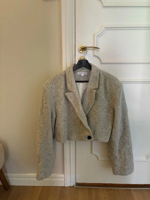 Grå croppad Adoore kavaj - Säljer en grå cropped kavaj från Adore med en oversized passform och en knapp framtill. Jackan har breda slag, lång ärm och är gjord i ett mjukt, strukturerat tyg som ger en trendig look. Perfekt att slänga över en t-shirt för en chill vibe. Aldrig använd, passar S/M