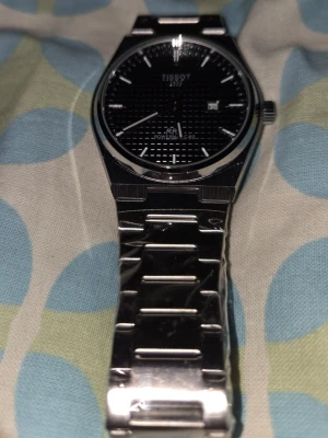 3 Tissot PRX silverklockor svart urtavla - Snygg Tissot PRX klocka i silver med länkarmband i metall och svart urtavla. Urtavlan har diskret rutmönster, datumvisning och tydliga visare. Klassisk och stilren design som passar till många olika looks.