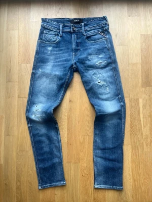 Replay Anbass W29 - Säljer dessa feta Replay Anbass i storlek W29 L30. Jeansen har många snygga slitningar men annars i fint skick, kom PM för mer info/bilder. Priset är ej hugget i sten!