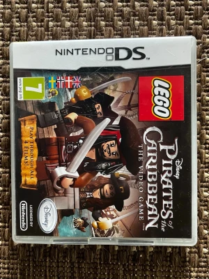 LEGO Pirates of the Caribbean DS-spel - Nintendo DS-spelet LEGO Pirates of the Caribbean: The Video Game. Omslaget har färgglada LEGO-figurer från filmen, med svärd och pirattema. Spelet är licensierat av Disney och Nintendo och har en tydlig LEGO-logga på framsidan.