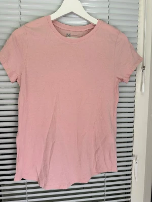 Ljusrosa t-shirt från FSBN Sister storlek: M - Enkel och stilren ljusrosa t-shirt från FSBN Sister. Klassisk rund halsringning och korta ärmar. Tillverkad i mjuk bomull som känns skön mot huden. Perfekt basplagg att matcha med jeans eller kjol.