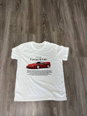 Vit Ferrari F40 t-shirt - Snygg vit t-shirt med tryck av en röd Ferrari F40 och text på bröstet. T-shirten har rund hals och korta ärmar, perfekt för dig som gillar bilar och vill ha en cool och unik stil.