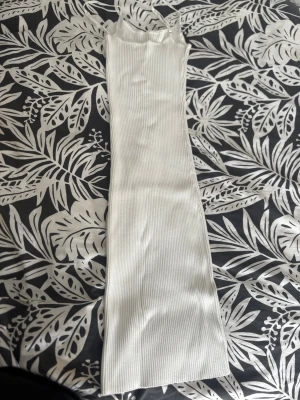 Vit ribbad långklänning - Säljer en vit ribbad långklänning med smala axelband och figurnära passform. Klänningen  har en enkel, stilren design som passar perfekt till sommaren. Materialet känns mjukt och stretchigt, vilket gör den bekväm att bära hela dagen. Den är i storlek M men rekommenderar klänningen ifall man har större storlek än M eftersom den är ganska stretchig