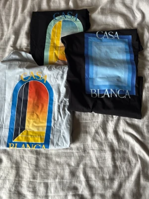 Casa Blanca grafiska t-shirts - Tre snygga t-shirts från Casa Blanca med grafiska tryck i olika färger. Två av tröjorna har ett fönsterliknande motiv i blått, gult, rött och svart, medan den tredje har ett blått fyrkantigt mönster. Alla är kortärmade och har en modern vibe. ALLTID SNÄLL VID SNABB OCH ENKEL AFFÄR💸