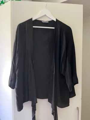 Svart kimono i tunn viskos - En svart kimono-inspirerad kofta med lös passform och långa ärmar. Tillverkad i ett tunt, mjukt tyg som ger ett flowy intryck. 