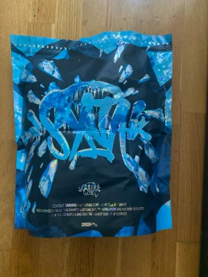 Svart hoodie från Syna world - Säljer en svart hoodie från Syna world med coolt graffiti-inspirerat tryck på bröstet. Hoodien har en klassisk huva och är tillverkad i ett mjukt material som passar perfekt för en avslappnad streetwear-look.