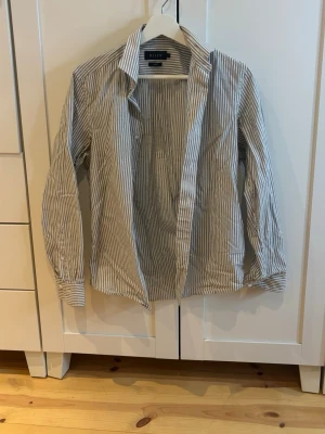 Randig skjorta från Riley, slim fit - Snygg vit skjorta från Riley med tunna blåa ränder och slim fit-passform. 