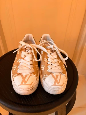 Beige Louis Vuitton sneakers - Snygga beige sneakers från Louis Vuitton med klassiskt monogrammönster i vitt. Skorna har vita snören, tjock vit sula och är tillverkade i läder. Perfekta för dig som vill sticka ut med exklusiva detaljer och trendig design.