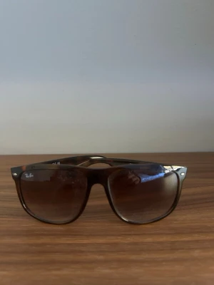 Bruna Ray-Ban solglasögon  - Snygga solglasögon från Ray-Ban i klassisk Wayfarer-modell. Bågarna är bruna med en lätt transparent finish och har Ray-Ban-loggan på sidan. Perfekta för att lyfta din stil med en tidlös look.