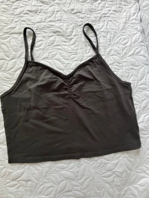 Mörkgrå croppad linnetopp H&M Divided - Säljer en mörkgrå croppad linnetopp från H&M Divided. Toppen har tunna axelband, lätt rynkning vid bysten och är tillverkad i mjuk bomull. Perfekt till sommaren och enkel att styla med olika outfits.