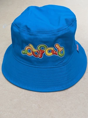 Bucket hat , Haribo - Cool blå bucket hat från Haribo med färgglatt godis motiv framtill och Haribo-logga på sidan. ONE SIZE 