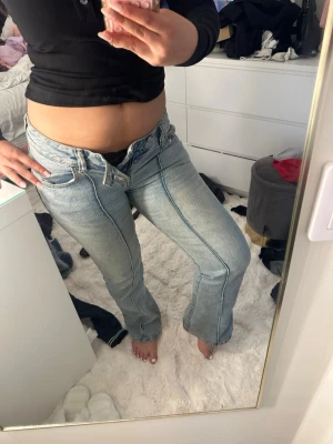 Ljusblå bootcut jeans med pressveck - Säljer ett par ljusblå bootcut jeans med markerade pressveck framtill. Jeansen har låg midja, klassiska fem fickor och stängs med dragkedja och knapp. Materialet är denim i bomull och de har en snygg tvättad look. Lite fläckar 