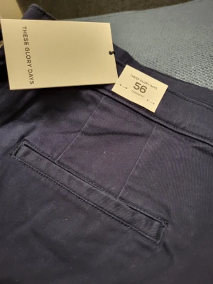 These Glory Days T Aimon Tapered mörkblå byxor, storlek 56 - Snygga mörkblå chinos från These Glory Days med klassisk rak passform och diskreta bakfickor. Materialet är mjukt och slitstarkt, perfekt för dig som vill ha ett stilrent och bekvämt plagg. Chinosen har hällor för bälte och knappstängning framtill.