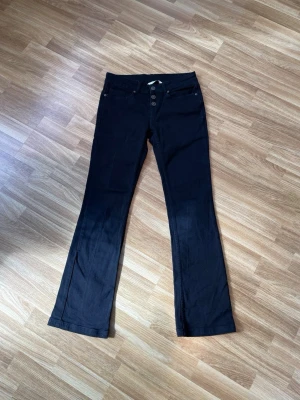Svarta bootcut jeans House of Lola - Snygga svarta jeans från House of Lola med bootcut passform och hög midja. Jeansen har knappgylf och klassiska fickor fram och bak. Perfekta för dig som gillar en tidlös och trendig look.