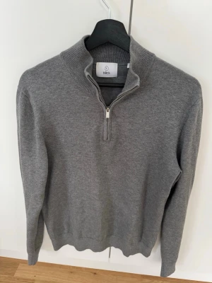 Grå halvzip-tröja från Bläck - Snygg grå stickad tröja från Bläck med halv dragkedja.Perfekt för lager-på-lager och enkel att matcha med jeans. Tröjan är i helt nytt skick.