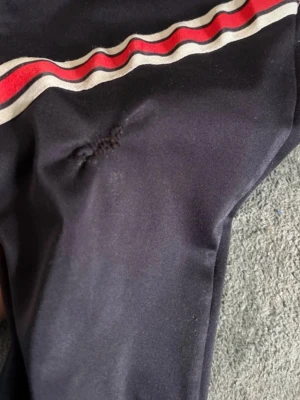 PSG x Jordan svarta mjukisbyxor - Svarta mjukisbyxor från PSG x Jordan med vita och röda ränder längs benen. Byxorna har elastisk midja, PSG-logga på ena benet och Jumpman-logga på andra. Tillverkade i ett mjukt syntetmaterial, perfekta för chill eller träning.