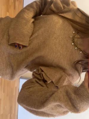 Beige tröja med volangärmar H&M - Beige stickad tröja från H&M med volangdetaljer på ärmarna. Tröjan är tillverkad i en mjuk blandning av polyester, akryl, ull och elastan. Perfekt för dig som gillar en trendig och mysig look.