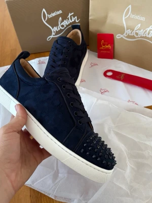 Mörkblå Christian Louboutin sneakers - Snygga mörkblåa Christian Louboutins med klassisk röd sula. Perfekta för dig som vill sticka ut med exklusiv design och detaljer. Storlek 42. Skriv om ni har mer frågor!
