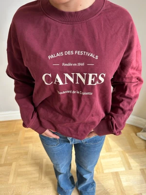 Vinröd sweatshirt med Cannes-tryck🌸💖💖 - Cool vinröd sweatshirt med vitt tryck på bröstet där det står 'Cannes' och 'Palais des Festivals'. Tröjan har rund halsringning, långa ärmar och är gjord i mjuk bomull. Perfekt för en avslappnad och trendig look.