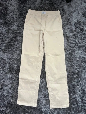 Beige chinos - Snygga beige chinos med rak passform och dragsko i midjan. Byxorna har sidofickor och är tillverkade i ett mjukt bomullsmaterial. Perfekta för en avslappnad och stilren look.