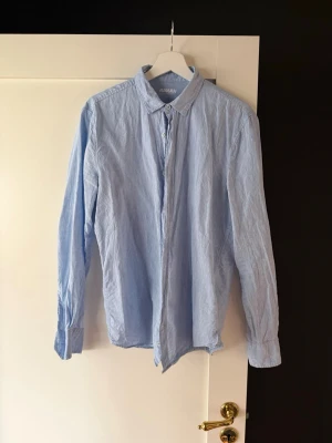 Linneskjorta  - Klassisk ljusblå skjorta i linne. Skjortan har lång ärm, knappar framtill och en stilren krage. Perfekt för en clean och enkel look. Passar till både jeans och kostymbyxor.