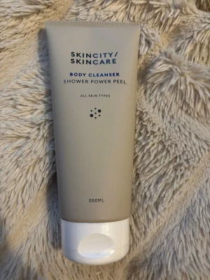 Skincity Skincare Body Cleanser 200ml - En duschpeeling för kroppen från Skincity Skincare. Tuben är beige med vit kork och rymmer 200 ml. Produkten är märkt 'Shower Power Peel' och passar alla hudtyper. Perfekt för dig som vill ha en fräsch och mjuk hud.