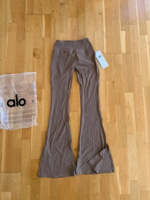 Beigea utsvängda leggings från Alo - Snygga beigea leggings från Alo med utsvängda ben och hög midja. Perfekta för en trendig och avslappnad stil. Diskret Alo-logga bak och medföljande originalpåse. Aldrig använda, har lappar kvar. Pris kan diskuteras vid snabb affär.