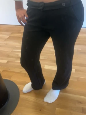 Svarta kostymbyxor med mid waist - Snygga svarta kostymbyxor med mid waist och knäppning fram. Byxorna har raka ben och sidofickor, samt ett dekorativt bälte i midjan. Perfekta för en stilren look. Materialet känns mjukt och följsamt.