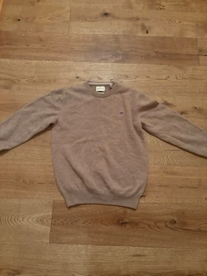 Beige stickad tröja från GANT - Säljer en beige stickad tröja från GANT i storlek M (passar mer som S). Tröjan har rund halsringning, ribbade muddar och en liten broderad logga på bröstet. Tillverkad i superfin ullblandning som känns mjuk och skön mot huden.