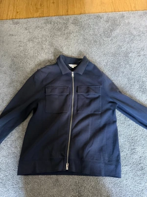 Mörkblå overshirt från Autograph - Stilren mörkblå overshirt från Autograph med två stora bröstfickor och dragkedja framtill. Klassisk krage och raka ärmar. Perfekt för lager-på-lager och enkel att matcha. Materialet känns mjukt och har en lätt struktur.