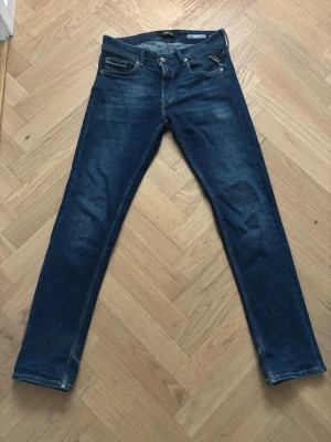 Mörkblå slim fit jeans från Replay - Snygga mörkblå straight fit jeans från Replay med klassisk femficksdesign. Jeansen har raka ben och detaljerade bakfickor med Replay-logga på läderpatch. Perfekta för en trendig och avslappnad stil.