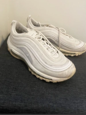 Nike Air Max 97 vita sneakers - Nike Air Max 97 sneakers i helvitt med ikoniska vågformade paneler och synlig Air-sula. Ovandelen är i textil och syntet med reflekterande detaljer och klassisk snörning. Snygg retrostil som passar till streetwear och casual outfits.