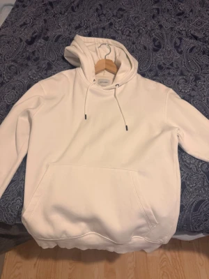 Vit hoodie från Jack & Jones - Snygg vit hoodie från Jack & Jones med klassisk känguruficka och dragsko i huvan. Hoodien har en enkel och clean design, perfekt för dig som gillar stilrena plagg. Tillverkad i mjukt material som känns skönt mot huden. Passar till det mesta i garderoben.