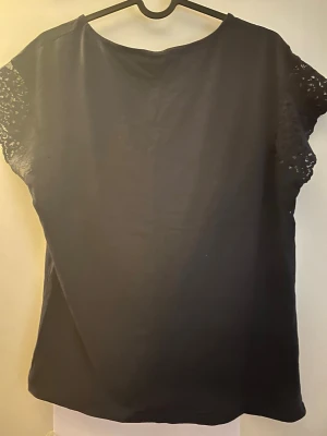 Marinblå blus med spetsärmar från Esprit - Marinblå blus från Esprit med korta ärmar i spets. Klassisk rund halsringning och rak passform. Perfekt för dig som gillar stilrena och enkla toppar med en twist av spetsdetaljer.