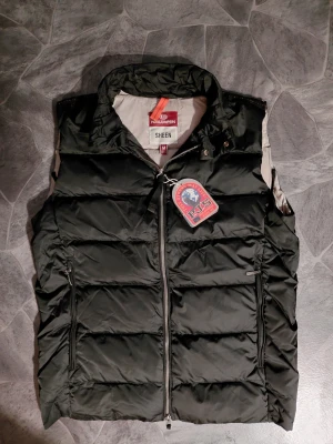 Svart dunväst från Parajumpers - Stilren svart dunväst från Parajumpers, modell Sheen. Västen har hög krage, två dragkedjeförsedda fickor och klassisk quiltad design. Märkets logga syns tydligt framtill. Perfekt för lager-på-lager och håller dig varm med lättviktig dunfyllning.