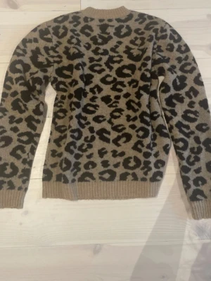 Leopardmönstrad stickad tröja - Snygg stickad tröja med leopardmönster i beige och svart. Tröjan har rund halsringning, långa ärmar och ribbstickade muddar vid ärmslut och nederkant. Perfekt för dig som vill sticka ut med ett trendigt djurmönster.