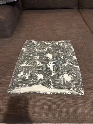 Kortkjol med svartvitt palmbladsmönster - Snygg kortkjol med svartvitt palmbladsmönster. Kjolen har rak passform och är tillverkad i mjuk bomull, perfekt för en avslappnad och trendig look. Mönstret ger en fräsch känsla och passar bra till både t-shirt och linne.